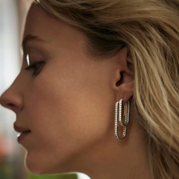 Close-up profile view of a person with long blonde hair wearing LAGOS Caviar Spark Linear Diamond Hoop Earrings, intricately designed and adorned with small gemstones. The background is softly blurred, highlighting the elegant jewelry.