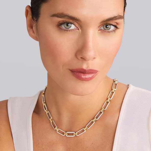 A person with fair skin, dark hair, and light eyes is wearing a white top and the LAGOS Signature Caviar Two-Tone Link Single Station Diamond Necklace. The background is plain and gray.