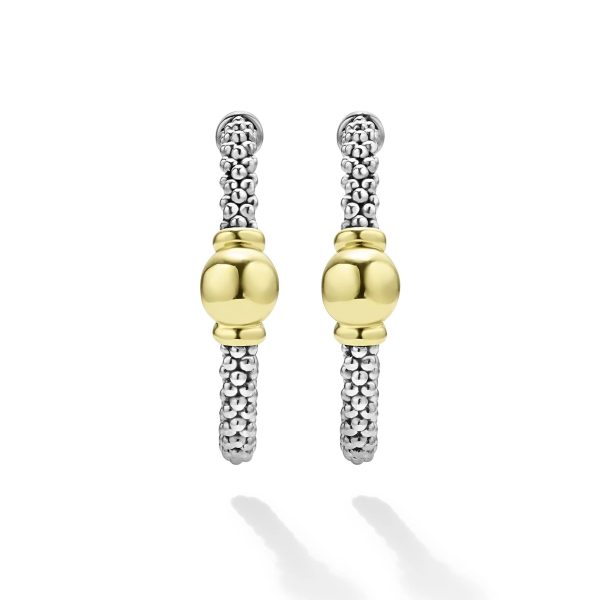 A pair of LAGOS Signature Caviar Two-Tone Station Hoop Earrings features hoops crafted from textured silver bands, each adorned with a central smooth gold sphere. These earrings boast a modern and elegant design by blending silver and gold elements seamlessly. The vertical arrangement of the hoops creates captivating shadow reflections against the pristine white background.