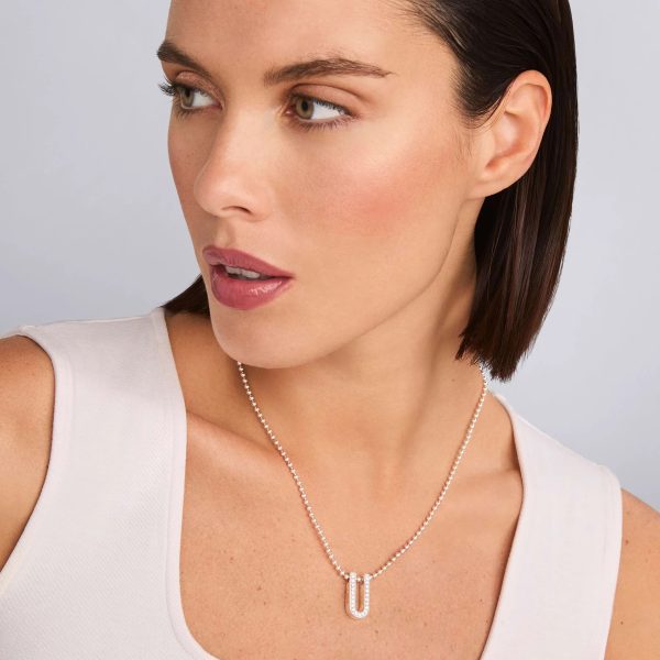 A person with short, straight brown hair and natural makeup looks to the side. They are wearing a sleeveless white top and the LAGOS Caviar Spark Large Linear Diamond Pendant Necklace. The background is light gray.