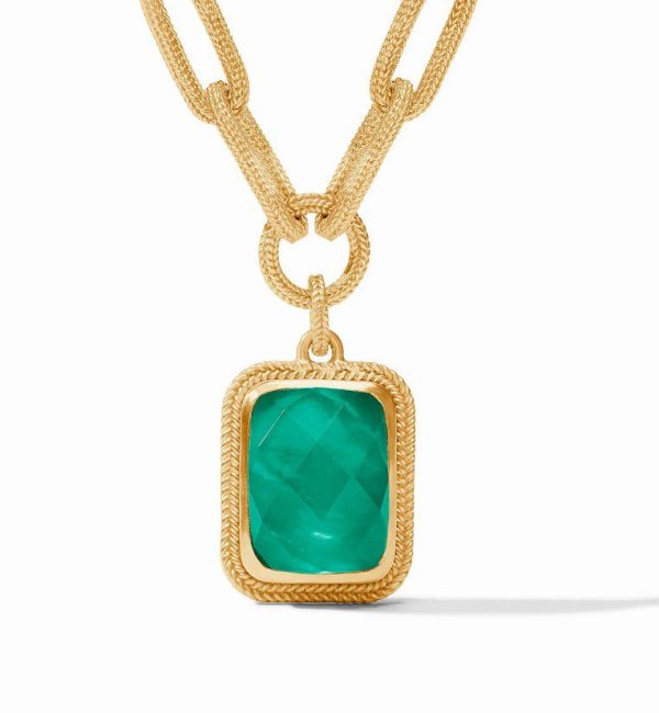 The Julie Vos Cheval Paperclip Statement Necklace in Iridescent Emerald Green boasts a dual chain design with a rectangular emerald-cut green gemstone pendant. The pendant is framed by a textured gold border, adding a touch of elegance to this luxurious accessory.