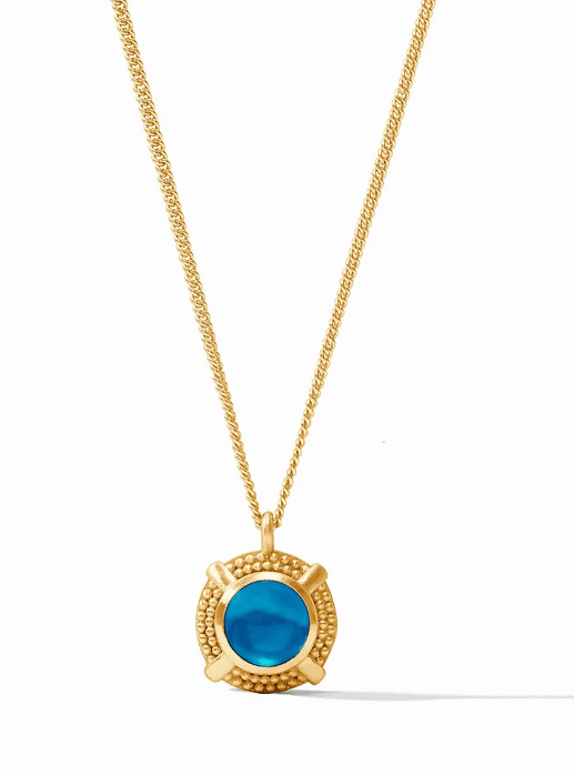 Presenting the Julie Vos Cabochon Solitaire Necklace - Iridescent London Blue, this gold necklace features a delicate chain and a round iridescent blue gemstone pendant set in an ornate gold bezel setting. The pendant showcases intricate detailing around the gemstone, with the image set against a plain white background.