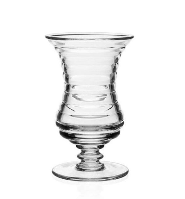 The William Yeoward Ripples Footed Vase - 6" showcases a clear, elegantly shaped glass design with a flared rim and concentric ridges adorning its body. It stands on a round, flat base, presenting an intricate pattern that exudes a layered and refined appearance against the plain white background.