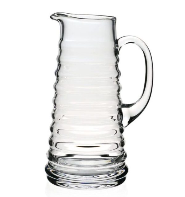 The William Yeoward Ripples Pitcher is a clear glass pitcher featuring a textured, ribbed body and a sturdy side handle. The design is sleek and minimalist, complemented by a slightly flared spout for easy pouring. The thick glass construction suggests durability.