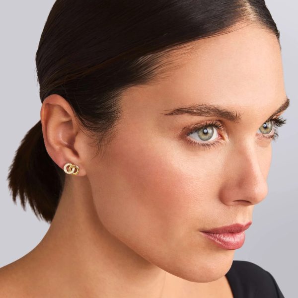 A person with light-colored eyes and dark hair tied back wears LAGOS Signature Caviar Two-Tone Interlocking Diamond Stud Earrings. The individual has a neutral facial expression and is dressed in a black top, with a light gray background.