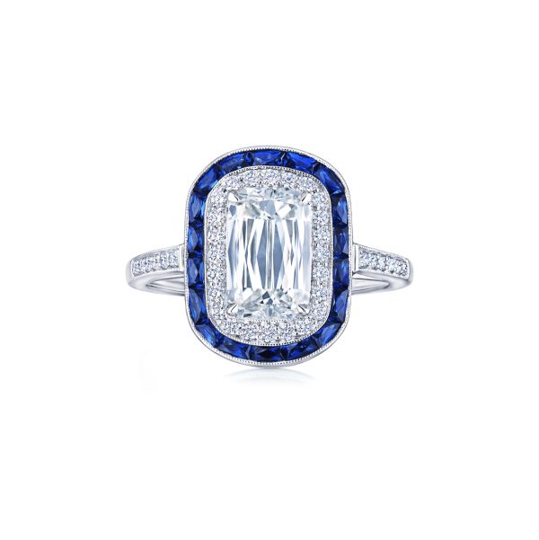 Introducing the Bromberg's Signature Collection Diamond Engagement Ring, showcasing a stunning large rectangular diamond encircled by shimmering smaller diamonds and vibrant blue sapphires in a double halo setting. The elegant band is adorned with dazzling diamond accents on each side.