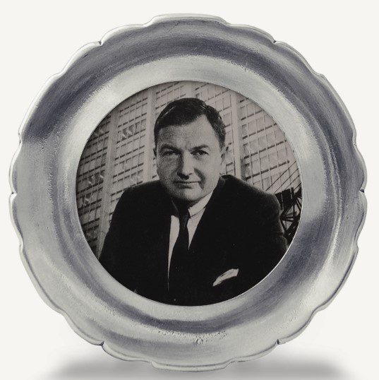 A black and white image depicting a man in a suit and tie, set against the backdrop of a large building with a grid-like structure, is elegantly encased in the MATCH Caretti Round Frame, featuring scalloped silver details.