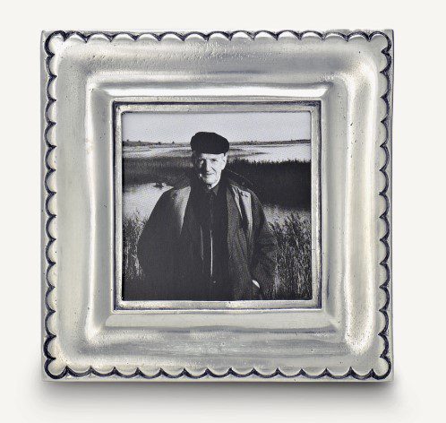 Black and white photo of a person in a cap and coat outdoors near water and reeds, displayed within the MATCH Trentino Frame featuring decorative scalloped edges.