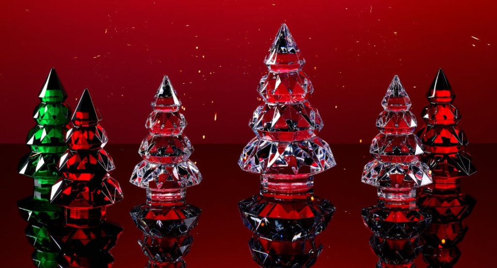 A group of five crystal trees, two green and three red, stand on a reflective surface with a deep red background. The trees are made of stacked, faceted crystal pieces tapering to a point, creating a sparkling effect.