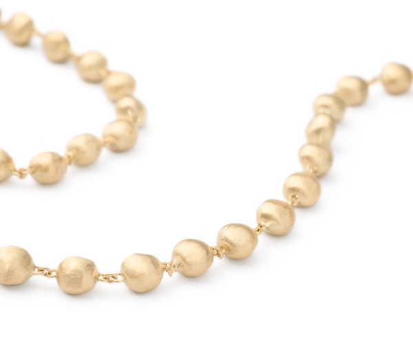 A close-up of the Marco Bicego Africa Yellow Gold Bead Necklace reveals spherical beads linked together. The surface of the beads is textured, giving them a matte appearance. The necklace is coiled, displaying part of its length against a white background.