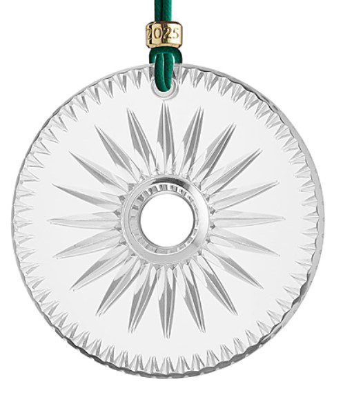 A round crystal ornament from Waterford, featuring a starburst design at the center and suspended from a green ribbon adorned with a gold bead engraved with "2023.