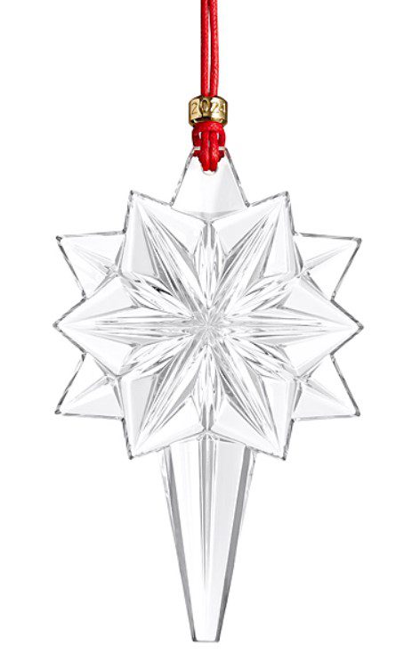 A Waterford 2024 Snow Star Ornament with intricate facets hangs from a red ribbon. It features a gold tag marked "2024" and includes a pointed crystal accent at the bottom.