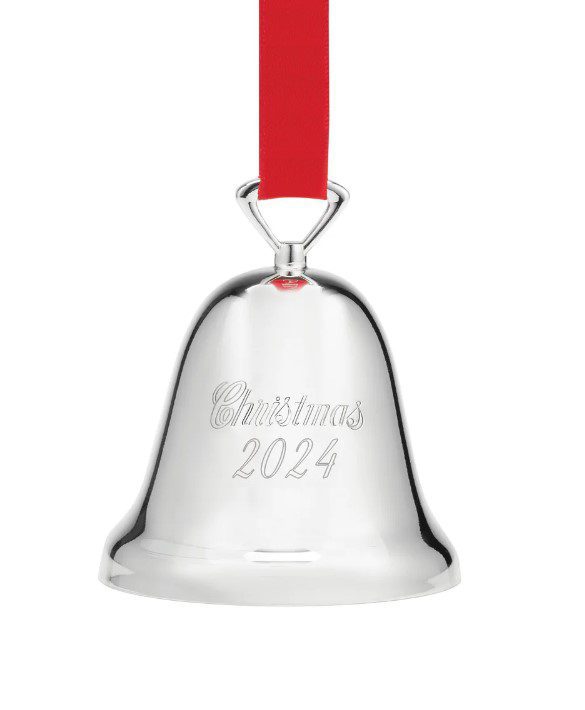 The Reed and Barton 2024 Christmas Bell Ornament, with its shiny silver finish engraved with "Christmas 2024," is showcased hanging from a vibrant red ribbon against a simple white background.