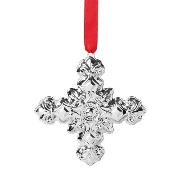 The Reed and Barton 2024 Cross Ornament is a shiny silver decorative piece with intricate detailing, hanging from a red ribbon.