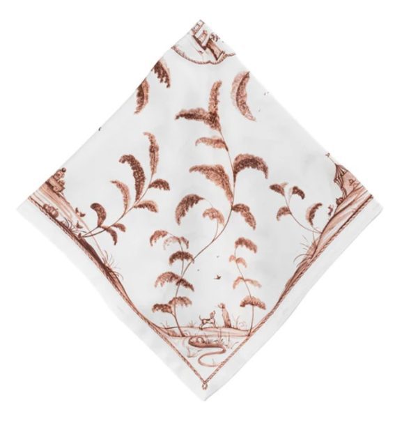 Introducing the Juliska Country Estate Harvest Napkin in Sepia: a square, white napkin adorned with an enchanting pastoral scene in brown, showcasing trees, animals, and rustic elements. The piece is beautifully bordered with intricate patterns.