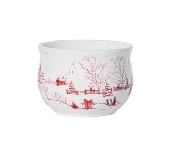 The Juliska Country Estate Winter Frolic Comfort Bowl is a white ceramic bowl adorned with red illustrations of a snowy landscape, showcasing trees, a fence, a small house, and scattered gifts.