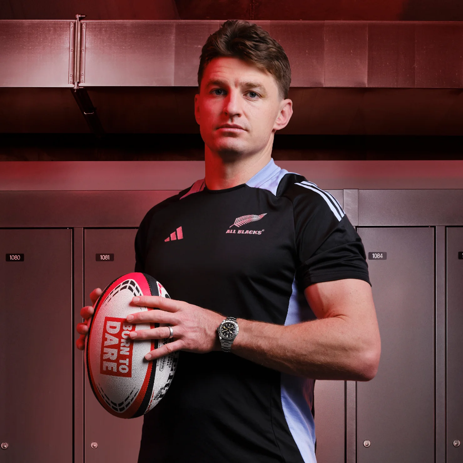 TUDOR Ambassador Beauden Barrett holding a rugby ball in his hands posing in front of lockers