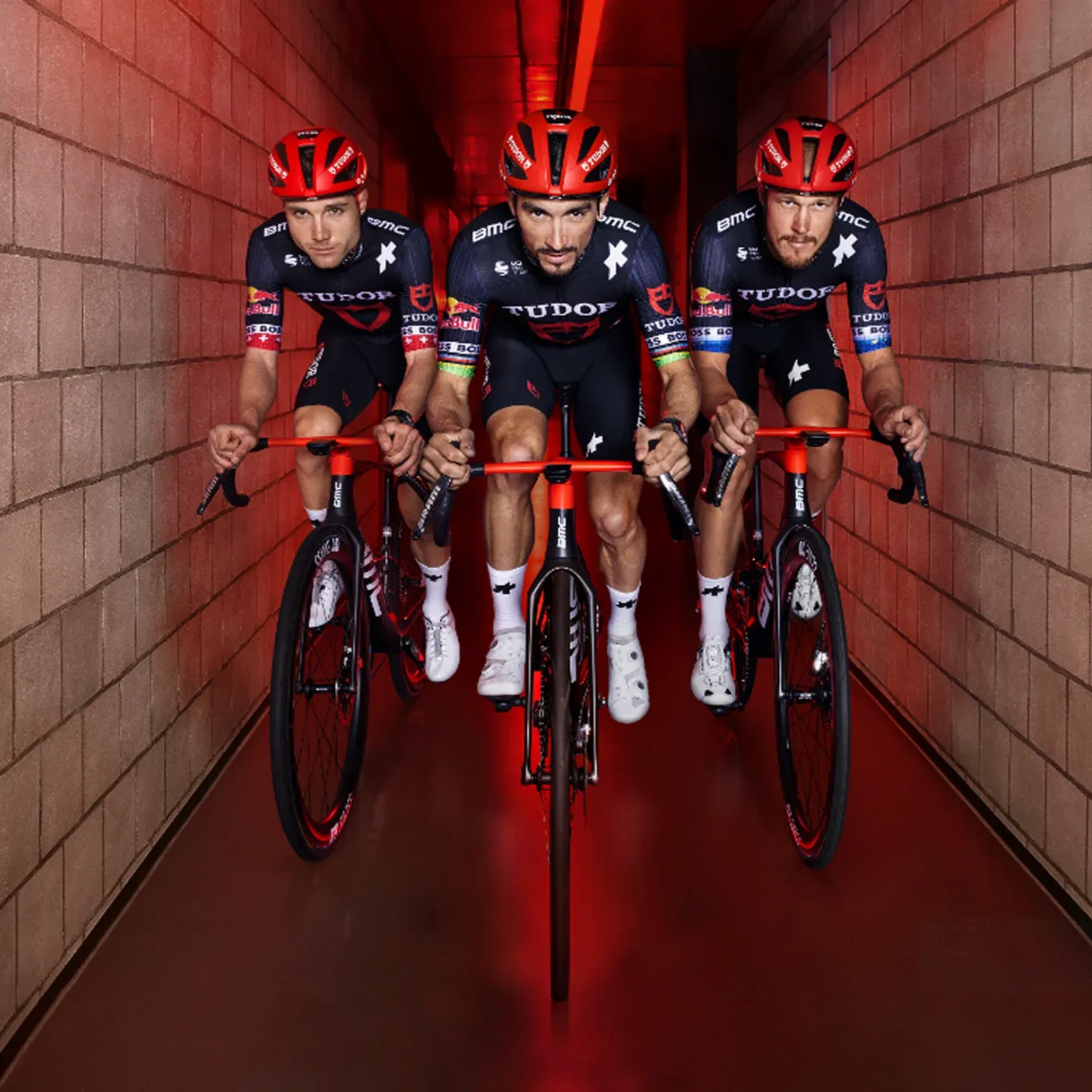 TUDOR Pro Cycling Team on bikes in hall with brick wall and red lighting